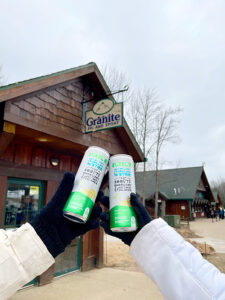 hands of two people who are not in frame holding cans of Bubblr in front of the Granite Ski and Sport building