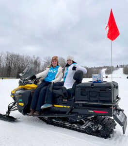 two women sitting on a snowmobile outdoors with a case of Bubblr sitting on the back