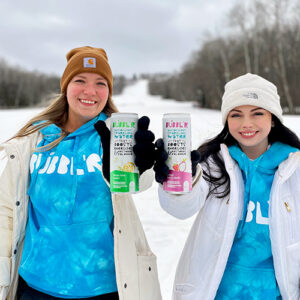 two woman outside in winter holding cans of Bubblr and smiling