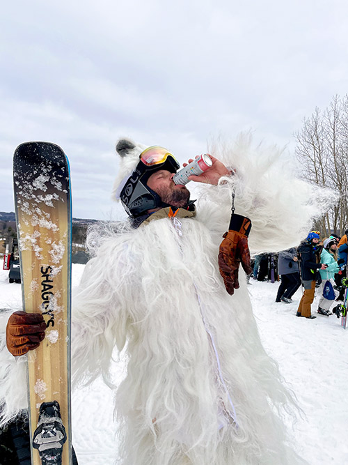 a man in yeti suit holding a snowboard in this right hand and drinking a can of Bubblr with his left hand