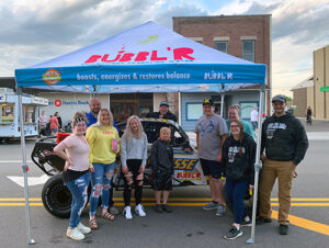 group of people posing outside on a street underneath a Bubbl'r branded tent with a Bubbl'r branded buggy behind them
