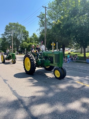 two people ride a green tractor with yellow wheels
