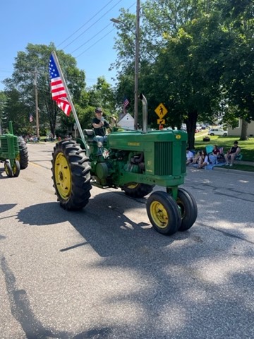 a person rides a green tractor with yellow wheels and an American flag