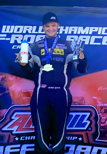 Mike Meister stands atop the winner's podium at the Pro Buggy 2022 Crandon World Championship holding a Bubbl'r bottle, and trophy