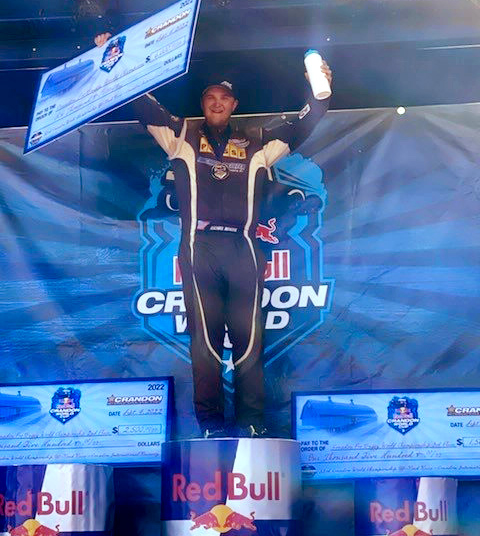 Mike Meister holds up an oversized check and Bubbl'r bottle atop the first place podium after winning the Pro Buggy 2022 Crandon World Championship