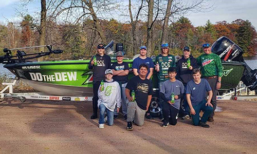 A group of 9 winners of the Take a Kid Fishing Contest pose in front of the boat with the fishing pro