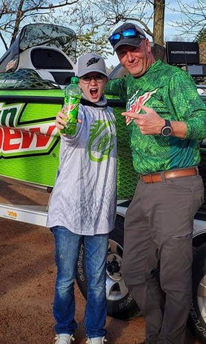 The Winner of the Take A Kid Fishing Contest poses with the Fishing Pro and holds a can of Mountain Dew