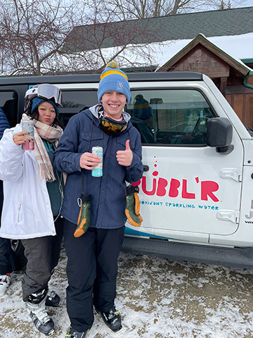 Granite Peak Bubblr Tasting holding cans in front of Jeep