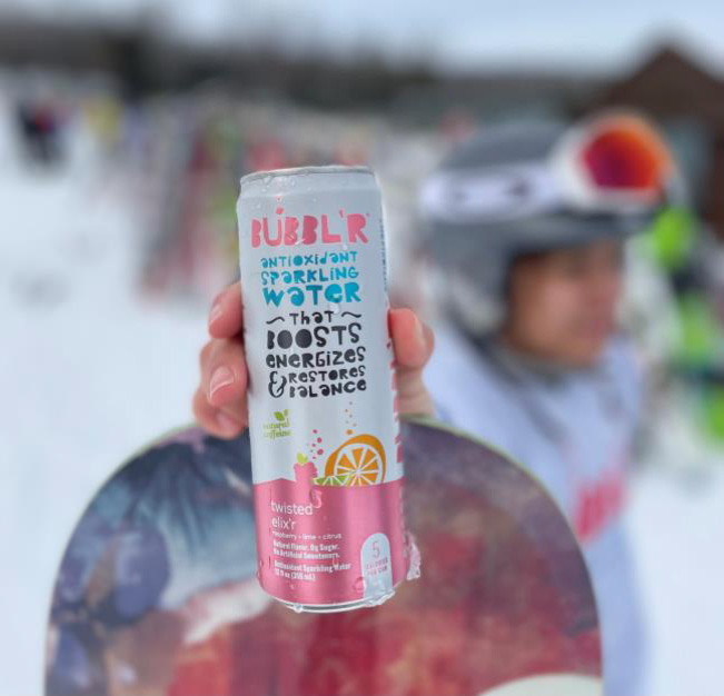 A snowboarder holds a can of Bubbl'r twisted elix'r on the top of her