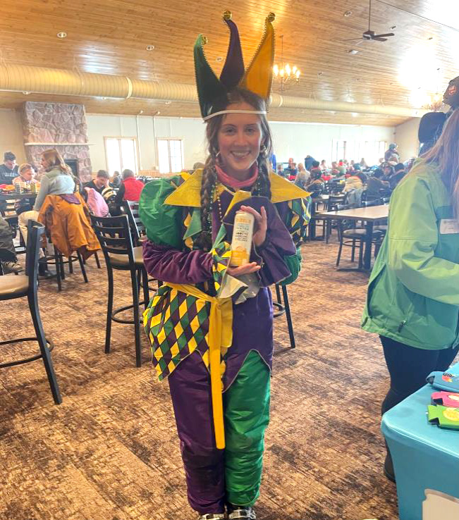 A young woman dressed in a purple, yellow and green Mard Gras outfit holds a can of Bubbl'r