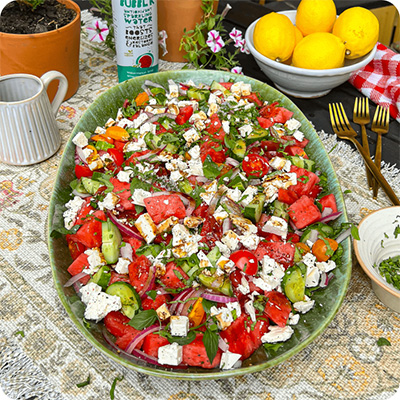 a can of Watermelon Bubb'r next to a watermelon, cucumber and feta summer salad